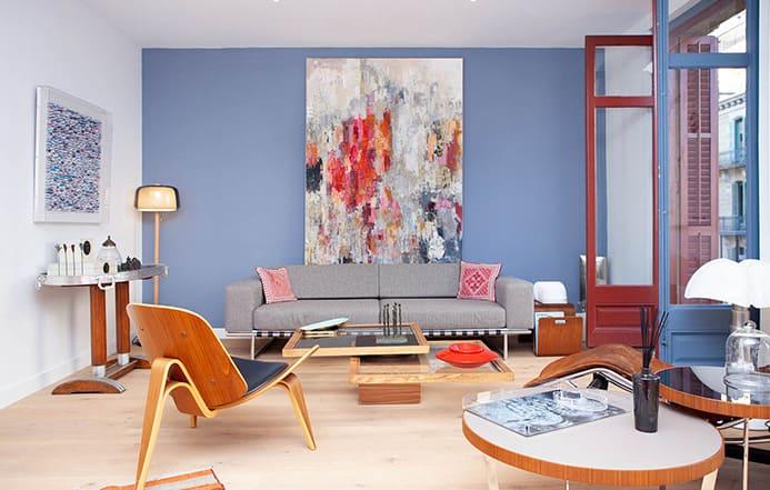 Salon moderne avec canapé gris, mur bleu et grande peinture colorée.