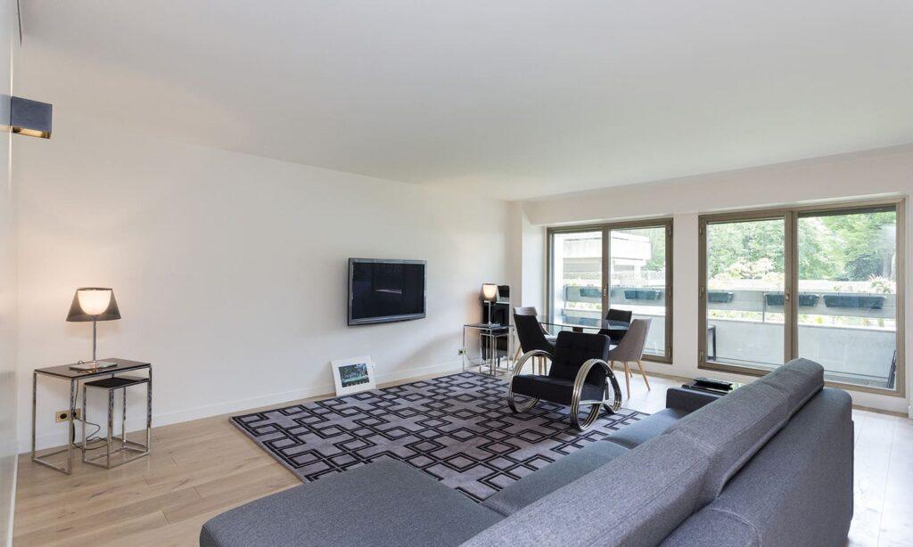 Salon moderne avec canapé gris et grandes fenêtres.