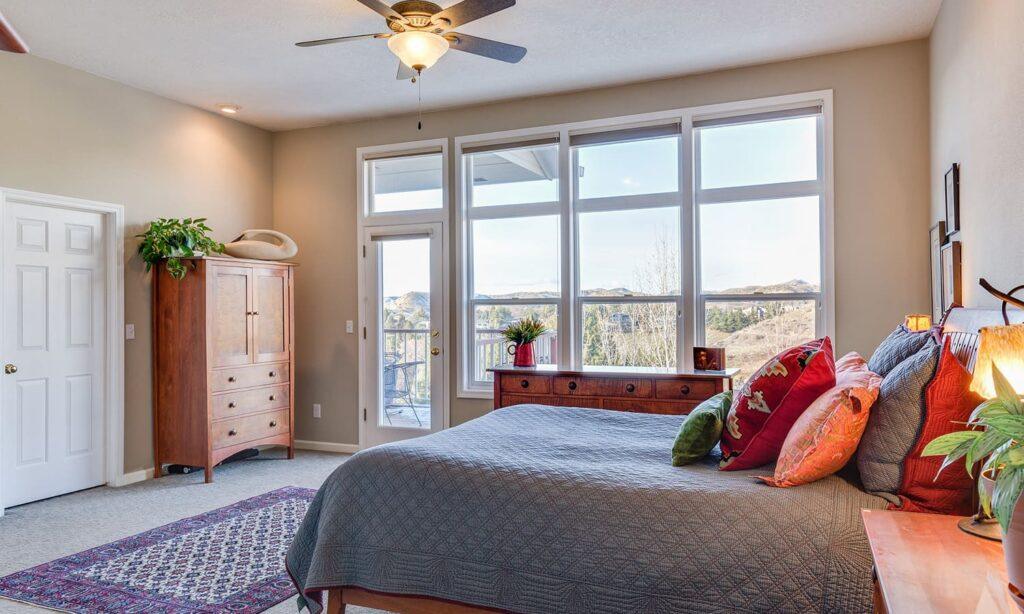 Chambre avec lit, armoire en bois et grande fenêtre offrant une vue extérieure.