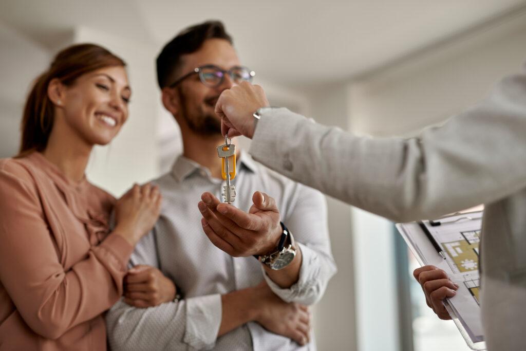 Agent immobilier remettant les clés d'une maison à un couple souriant.