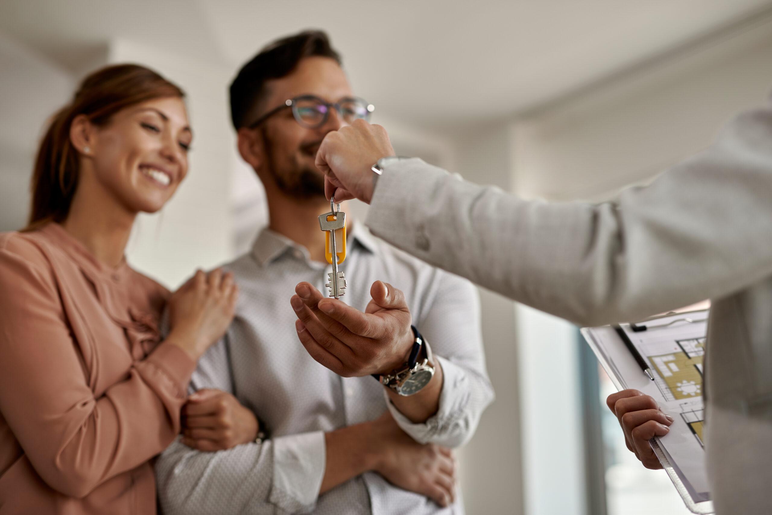 Agent immobilier remettant les clés d'une maison à un couple souriant.