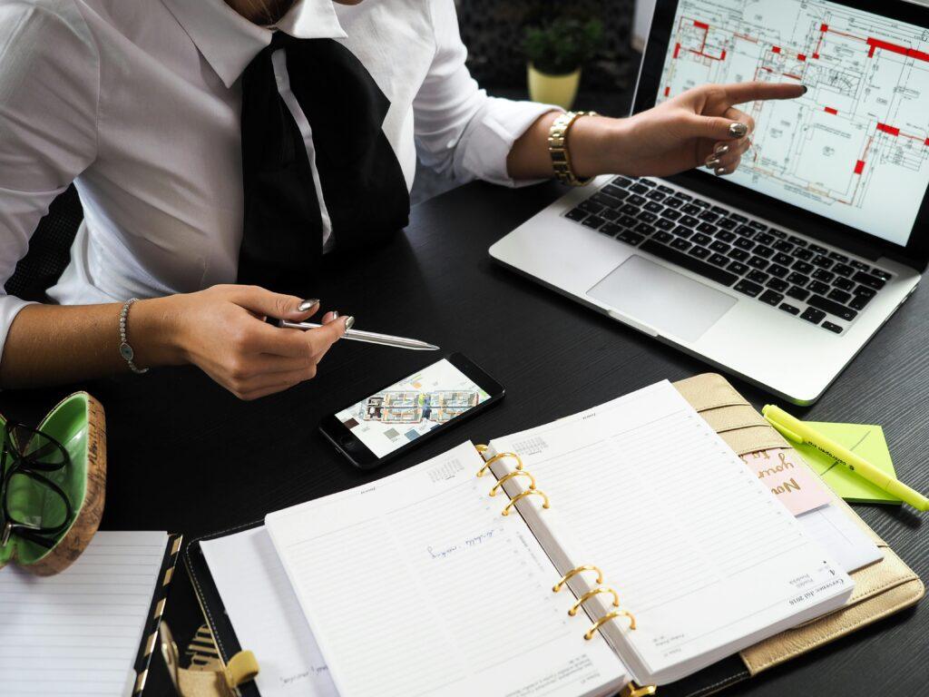 Personne travaillant sur des plans architecturaux avec un ordinateur portable et un agenda.
