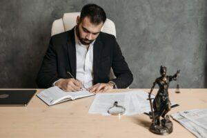 pexels pavel danilyuk Homme en costume écrivant à un bureau avec une statue de justice.