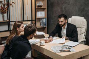 pexels pavel danilyuk Un homme en costume discute de documents avec un couple dans un bureau.