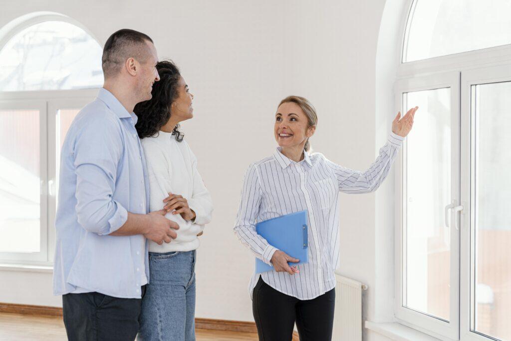 smiley female realtor showing empty house young couple () Agent immobilier souriant montrant une maison vide à un jeune couple.