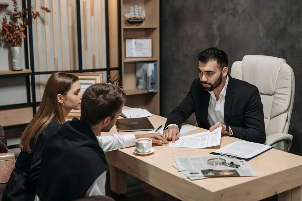 Un homme en costume discute avec un couple dans un bureau.