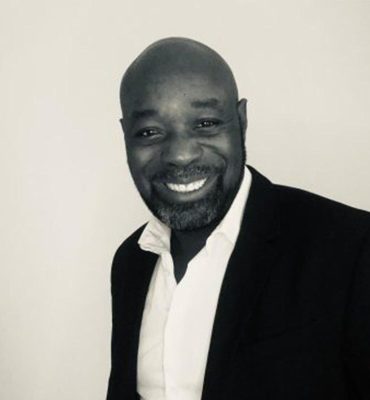 Eric Mpome Je ne sais pas qui est sur l'image. Voici une suggestion pour le texte alternatif : "Homme souriant en costume noir et chemise blanche."